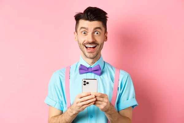 Online nakupování. Šťastný muž vypadá ohromeně po přečtení obrazovky smartphone, usmívá se vzrušeně do kamery, stojí nad růžovým pozadím — Stock fotografie