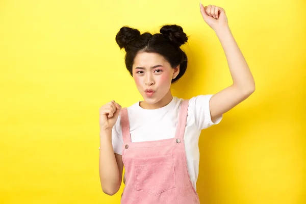 Eccitato asiatico donna ottenere motivazione, alzando la mano e cantando, celebrando la vittoria, trionfante e in piedi su sfondo giallo — Foto Stock