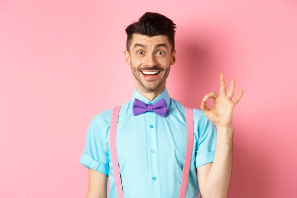 Красивий білий чоловік з вусами посміхається і показує добре знак, схвалює щось хороше, хвалячи відмінний вибір, що стоїть розважаючись на рожевому фоні — стокове фото