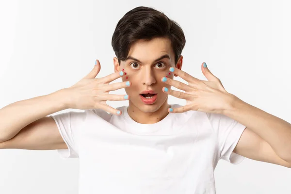 People, lgbtq and beauty concept. Close-up of beautiful gay man with glitter on face, showing nail polish on his fingernails, looking sassy at camera, standing over white background — Stock Photo, Image