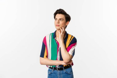 Sol üst köşeye bakan angrodynous genç adam görüntüsü düşünceli, tanıtım okuyor, beyaz arka planda duruyor.