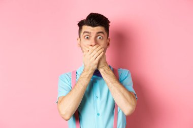Şok olmuş ve nutku tutulmuş adam ağzını kapattı, elleriyle dudaklarını kapadı ve kameraya baktı, pembe arka planda duruyordu.
