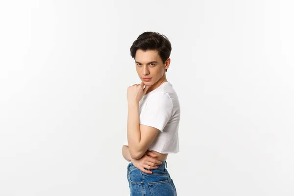Lgbtq and pride concept. Side view of attractive androgynous man in crop top looking sassy at camera, standing over white background — Stock Photo, Image