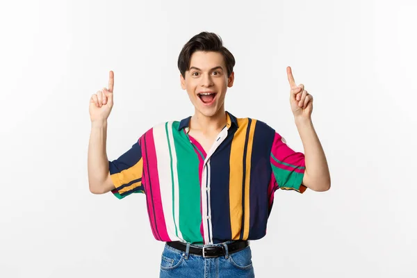 Happy attractive gay man pointing fingers up, smiling excited, showing top offer, standing over white background — Stock Photo, Image