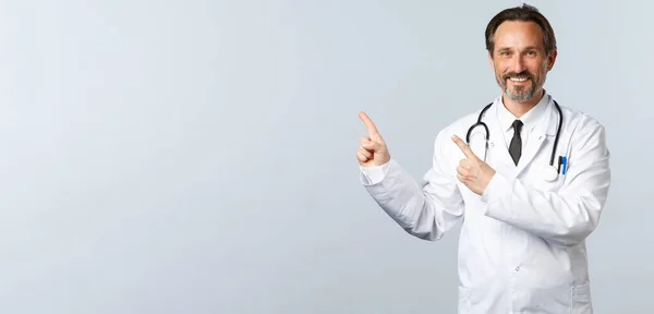 Covid-19, coronavirus outbreak, healthcare workers and pandemic concept. Smiling friendly-looking doctor in white coat pointing fingers upper left corner, showing advertisement — Stock Photo, Image