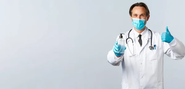 Covid-19: 바이러스 예방, 의료 종사자 및 예방 개념. 의료용 마스크를 착용하고 장갑을 낀 의사의 승인을 받아 손 소독 전문가와 흰 배경 사진을 추천 한다. — 스톡 사진
