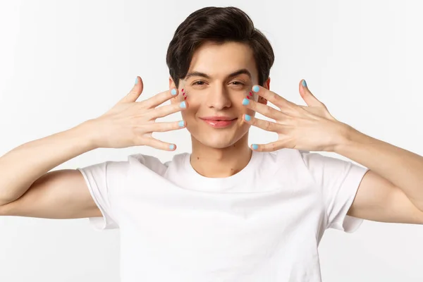 People, lgbtq and beauty concept. Close-up of beautiful gay man with glitter on face, showing nail polish on his fingernails, looking sassy at camera, standing over white background — Stock Photo, Image