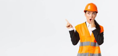 Şaşırmış ve etkilenmiş Asyalı kadın mühendis, güvenlik kaskı ve yansıtıcı ceketli inşaat müdürü, sol üst köşesinde nefes nefese kalmış parmak, hayrete düşmüş, ilginç bir şey buldu.