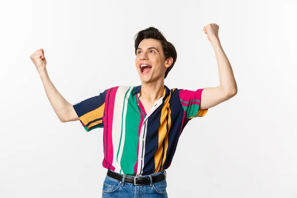 Happy gay man celebrating victory, raising hands up and rejoicing of winning, tirumphing while standing over white background — Stock Photo, Image