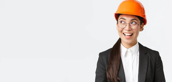 Detailní záběr kreativní asijské architektky se zajímavým nápadem, stavební inženýr v obleku a bezpečnostní přilba při pohledu vlevo s potěšeným úsměvem, stojící bílé pozadí — Stock fotografie