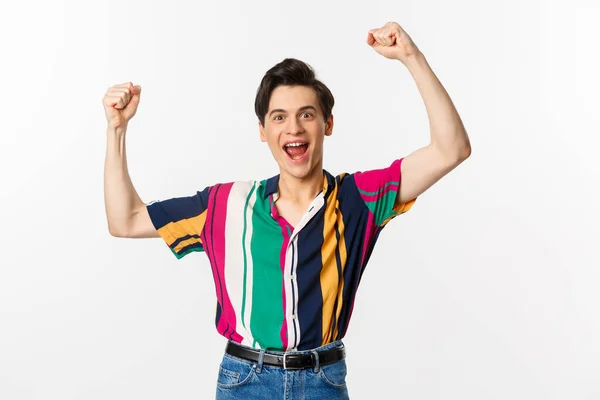 Image of happy young man triumphing of winning, celebrating victory, raising hands up in rejoice and shouting yes, standing over white background — Stock Photo, Image