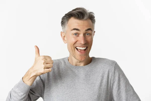 Primer plano de alegre hombre de mediana edad, sonriendo feliz y satisfecho, mostrando pulgares hacia arriba, expresando su aprobación, como algo bueno, de pie sobre fondo blanco — Foto de Stock