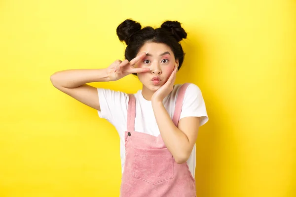 Kawaii ασιατικό κορίτσι δείχνει v-σημάδι και κατσούφιασμα χαριτωμένο, κάνοντας ανόητο πρόσωπο με μακιγιάζ, στέκεται σε κίτρινο φόντο — Φωτογραφία Αρχείου