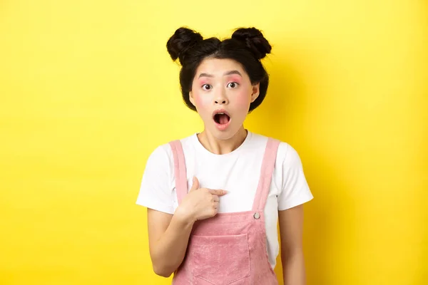Sorprendido asiático adolescente chica con glamour maquillaje, apuntando a sí misma y jadeando confundido, siendo elegido o acusado, de pie sobre fondo rosa —  Fotos de Stock