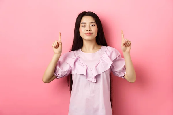 Sonriente adolescente chica asiática señalando los dedos hacia arriba en el espacio vacío, publicidad sobre fondo rosa —  Fotos de Stock