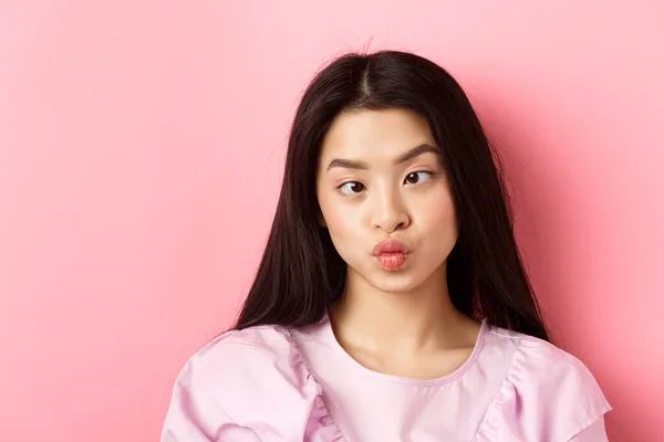 Primer plano retrato de divertido asiático mujer entrecerrando los ojos y haciendo tonto caras, de pie sobre rosa fondo —  Fotos de Stock