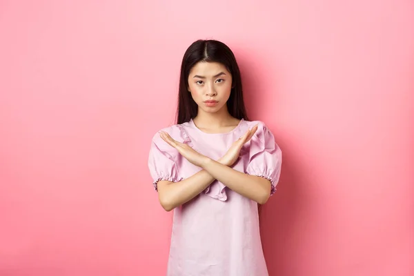 Σοβαρή κινεζική κορίτσι δείχνουν σταυρό σημάδι, κάνουν χειρονομία στάση και να εξετάσουμε σίγουροι, μπλοκ πρόσωπο, να πω όχι και να απορρίψει την προσφορά, στέκεται σε ροζ φόντο — Φωτογραφία Αρχείου
