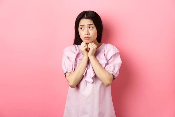 Aggódó félénk ázsiai lány néz félre, kézen fogva nyomja a mellkasát, és úgy néz ki, aggódik, álló szomorú és komor fehér háttér — Stock Fotó