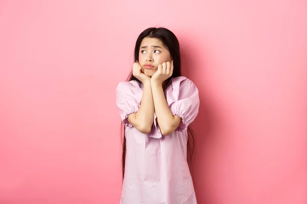 Szomorú és magányos ázsiai lány néz balra, és ráncolja a homlokát, álló szomorú ellen rózsaszín háttér — Stock Fotó