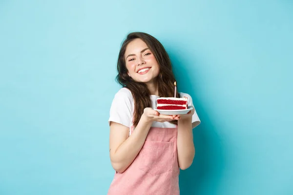 Fiestas y celebración. Linda chica glamour celebrando su cumpleaños, sosteniendo el plato con pastel y sonriendo alegre, celebrando, de pie sobre fondo azul — Foto de Stock