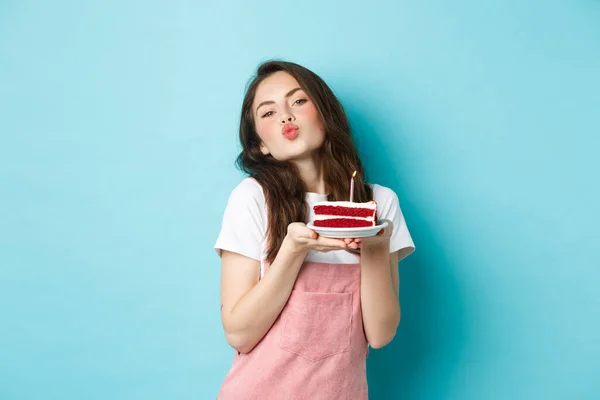 Fiestas y celebración. Linda chica tonta pidiendo deseo en pastel de cumpleaños, haciendo cara de beso, celebrando b-day, de pie alegre sobre fondo azul —  Fotos de Stock