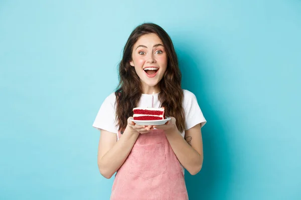 Férias e conceito de festa. Garota bonita excitada soprando vela no bolo de aniversário, celebrando seu dia-b, de pé sobre o fundo azul — Fotografia de Stock