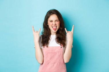 Bu olay yıkılıyor. Şımarık ve heyecanlı genç kadın eğleniyor, rock-n-roll işaretleri gösteriyor ve evet diyor, konserin tadını çıkarıyor, mavi arka planda duruyor.