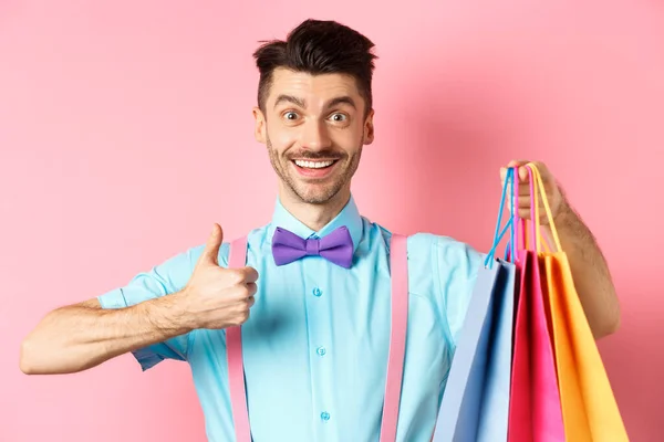 Comprador masculino feliz mostrando pulgares hacia arriba y bolsas de compras, recomendando tienda, de pie sobre fondo rosa —  Fotos de Stock