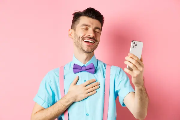 Concetto tecnologico. Felice uomo caucasico video chat e ridere di smartphone, in piedi su sfondo rosa — Foto Stock