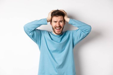 Hüsrana uğramış genç adam panik içinde çığlık atıyor, beyaz arka planda endişeli duruyor, panikliyor.