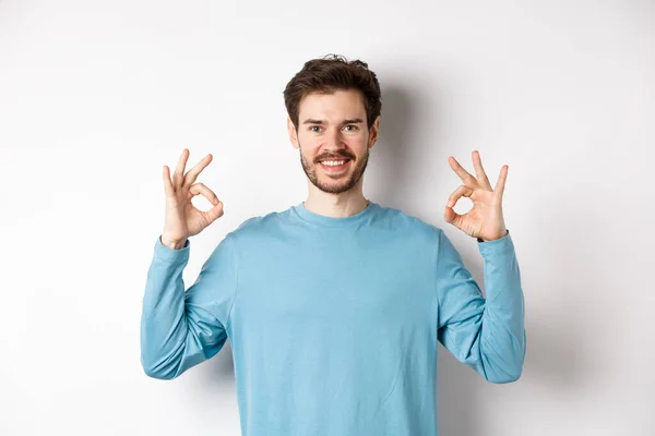 Very good. Smiling handsome guy showing okay signs and looking satisfied, standing over white background, approve excellent choice — Stock Photo, Image