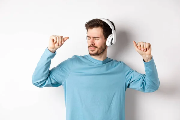 Jovem feliz se divertindo em fones de ouvido, dançando enquanto ouve música em fones de ouvido sem fio, fundo branco — Fotografia de Stock