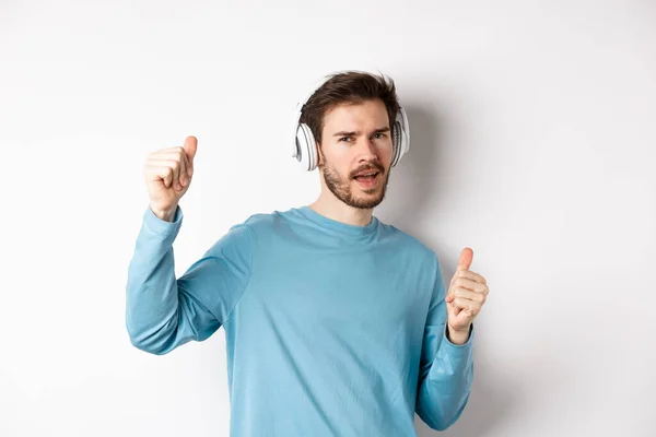 Θρασύς τύπος που χορεύει και διασκεδάζει με ασύρματα ακουστικά, απολαμβάνοντας καλή ποιότητα ήχου, λευκό φόντο — Φωτογραφία Αρχείου
