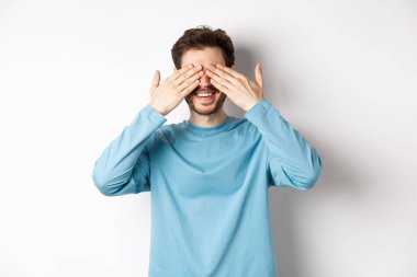 Gülümseyen beyaz adam sürpriz bekliyor, gözleri kapalı, hediye bekliyor, beyaz arka planda duruyor. Kutlama ve tatil kavramı