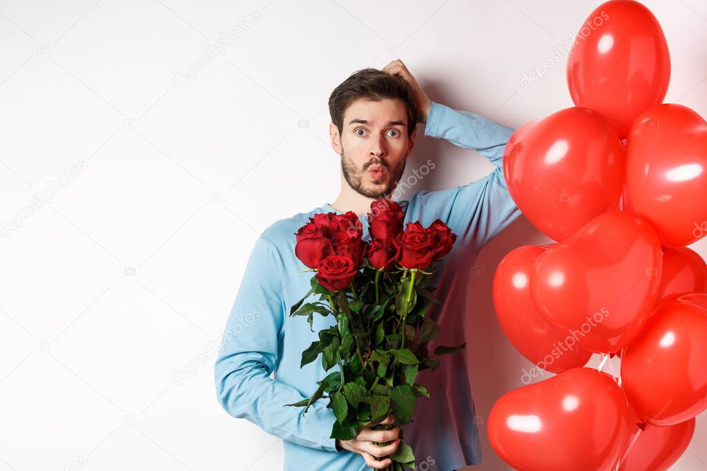 Valentines day romance. Worried boyfriend holding bouquet of red roses and red heart balloons, scratching head and looking anxious, going on romantic date, white background