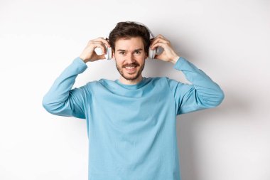 Adam müzik ya da podcast dinlemek için kablosuz kulaklık takmış, kameraya gülümsüyor, pembe arka planda duruyor.