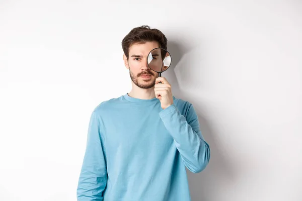 Man söker efter något, tittar igenom förstoringsglas på kameran, står på vit bakgrund — Stockfoto