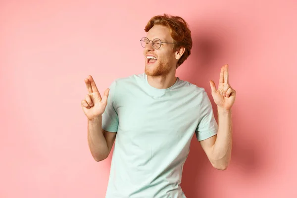 Glada rödhårig kille lyssnar musik och dans, triumferar eller firar framgång, står över rosa bakgrund — Stockfoto