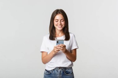 Gülümseyen çekici kız cep telefonu kullanıyor ve ekrana bakıyor.