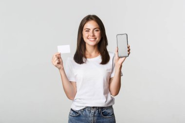 Çekici gülümseyen kız memnun görünüyor ve kredi kartı, cep telefonu ekranı gösteriyor.