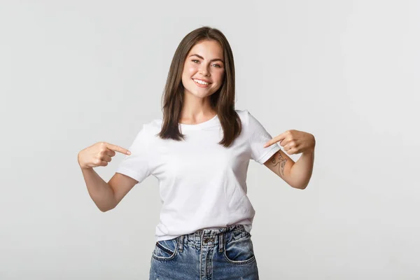 Attraente ragazza bruna sorridente che indica il tuo logo, mostrando banner al centro — Foto Stock