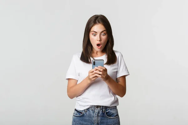 Scioccato e impressionato ragazza bruna guardando stupito lo schermo dello smartphone — Foto Stock