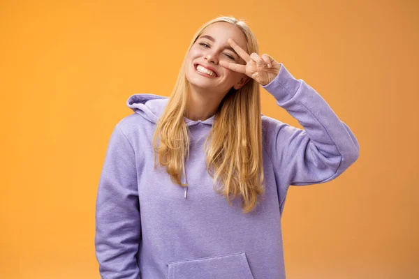 Despreocupado optimista joven linda rubia caucásica novia divertirse disfrutando del sol perfecto primavera tiempo guiño descarado sonriente inclinación cabeza alegremente mostrar paz victoria signo, fondo naranja — Foto de Stock