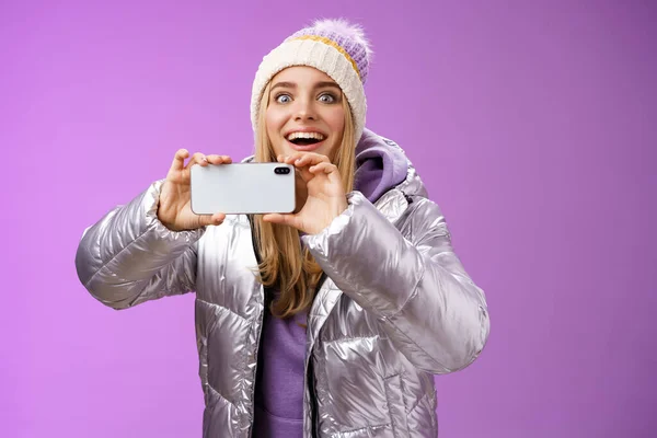 Amüsiert faszinierte Frau in silberner Jacke Kopf lächelt erstaunt aufgeregt Blick nach vorne halten Smartphone Aufnahme Video Aufnahmen berühmte Person Handykamera, lila Hintergrund — Stockfoto