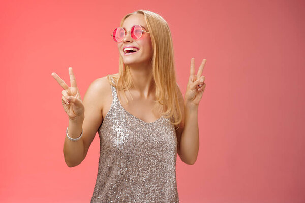 Positive charming european carefree stylish girlfriend having fun dance-floor show victory signs look up happily smile in sunglasses glamour gllittering dress enjoy celebration, red background