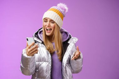 Rahatsız edici şikayetler, tatminsiz sarışın kız, aptal akıllı telefon diye bağırıyor, mutsuz bir şekilde mızmızlanıyor, cep telefonu sesi kaydediyor, üzgün, mor arka planda duruyor.