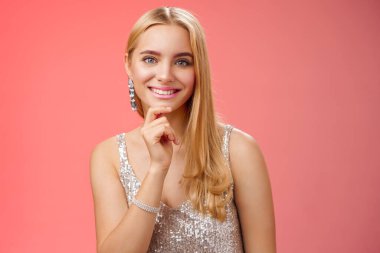 Yakın plan sevimli sarışın kız gümüş renkli parti elbisesi giyiyor gülümsüyor dostça gülümsüyor ilginç sohbetler yapıyor kırmızı arka planda eğleniyor, eğleniyor.