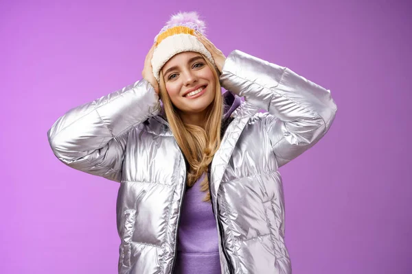 Zarte romantische attraktive blonde Frau genießen Winterurlaub Skigebiet Spaß Aussehen erfreut lächelnd breit geneigten Kopf berühren Hut trägt silberne Jacke, lila Hintergrund — Stockfoto