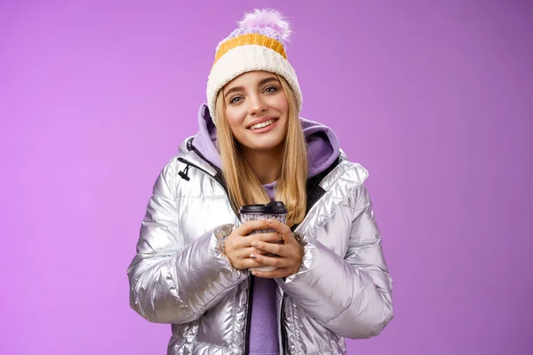 Zart entspannt fröhlich lächelnd blondes Mädchen schauen zufrieden erleichtert Kaffee trinken Kakao genießen schönen herzerwärmenden Moment Blick Kamera erfreut sanftes Grinsen, trägt Winterjacke Hut — Stockfoto