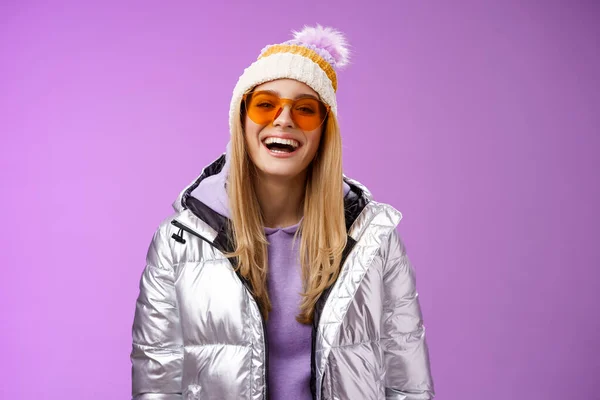 Stylový přátelský charismatický blond žena ve stříbře lesklé bundy klobouk sluneční brýle připraven naučit snowboarding s úsměvem šťastně se baví zasněžené rekreační resort, stojící fialové pozadí — Stock fotografie
